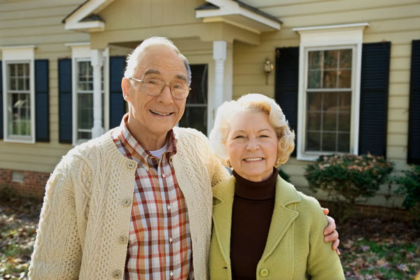 smiling senior couple standing in front of home